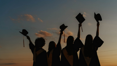 Image of four graduating students raising their caps in the air.