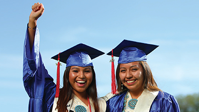 Image of two  female Native American graduates wearing cap and gown