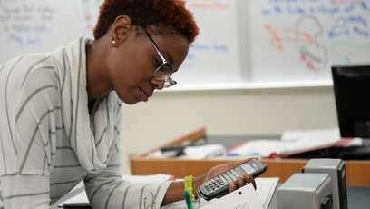 Image of woman wearing glasses and a stripped sweater using a calculator and writing in a notebook