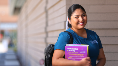 An image of a smiling woman wearing nursing scrubs and holding nursing textbooks