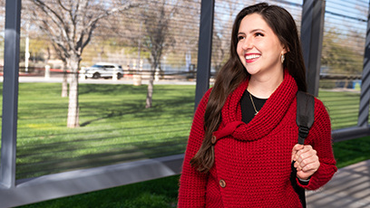 A happy, smiling student wearing a red sweater and backpack standing outside