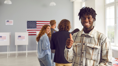 An African American man smiling and giving a thumbs up at an election polling location
