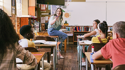 Teacher in classroom sitting on desk, speaking to group of students 
