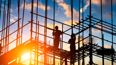 Stock photo of construction workers standing on scaffolding as the sun rises
