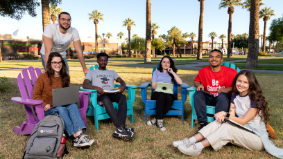 Four GCC students sitting outside in chairs and one sitting on the grass at the college campus