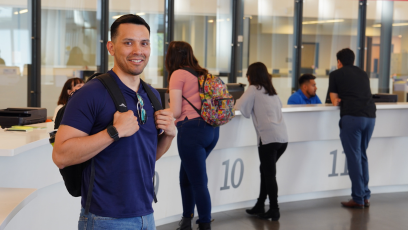 An image of a MCC student wearing a backpack standing in the college's enrollment center with students standing behind him at being helped by enrollment staff.