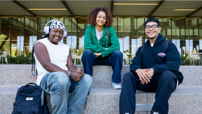 Three EMCC students sitting on steps outside of an entrance of a college building.