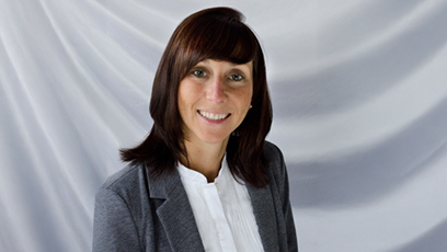 A gray background with a smiling Beth Roszatycki wearing a dark gray suit jacket and a white blouse.