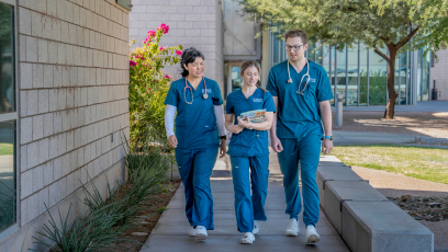 Three CGCC allied health students wearing blue medical scrubs walk together on the college campus.