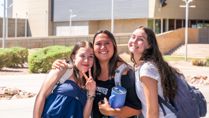 Three female college students standing together outside at a campus.