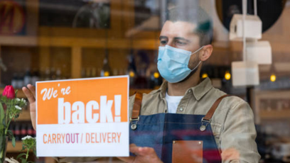 Shop owner holding up sign that reads, "We're back!"