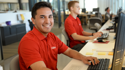 Image of two Mesa Community College students using computers and  wearing red polo shirts