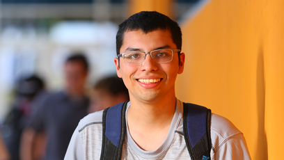 Image of a smiling male student wearing a gray T-shirt and navy backpack