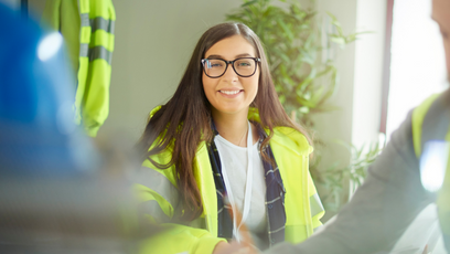 Image of a female construction worker how appears in focus with a male construction in the foreground 