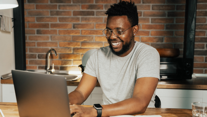 A man wearing a grey T-shirt working on a laptop