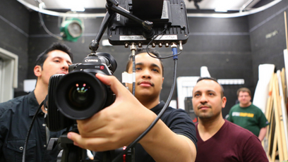 Image of three photo journalist student using a camera with a fourth person in the background