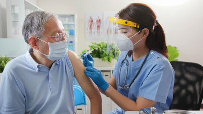 Image of a woman healthcare professional wearing PPE giving a vaccine to a elderly man