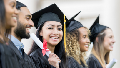 A group of college graduates wearing caps and gowns and one woman holding a diploma and smiling