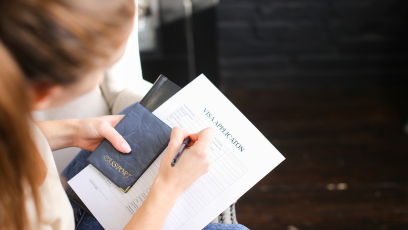 An image of a woman holding a passport and completing Visa form