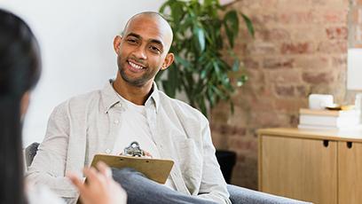 An image of a smiling male holding a clipboard listening to a woman
