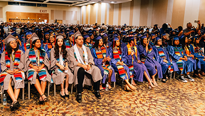 Room of students wearing cap and gowns during graduation ceremony.