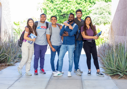 Six college students standing together outside wearing backpacks and holding books