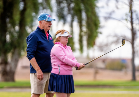 Joe Bockerstette standing bending his daughter Amy Bockerstette who is holding a golf club.