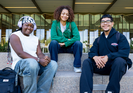 Three EMCC students sitting on steps outside of an entrance of a college building.