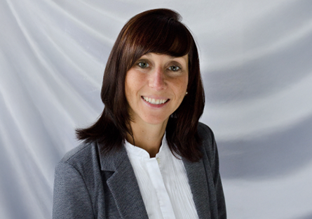 A gray background with a smiling Beth Roszatycki wearing a dark gray suit jacket and a white blouse.
