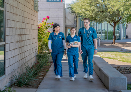 Three CGCC allied health students wearing blue medical scrubs walk together on the college campus.