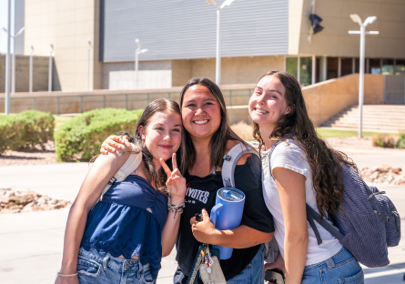 Three female college students standing together outside at a campus.