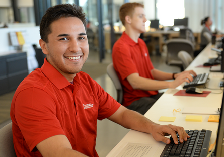 Image of two Mesa Community College students using computers and wearing red polo shirts