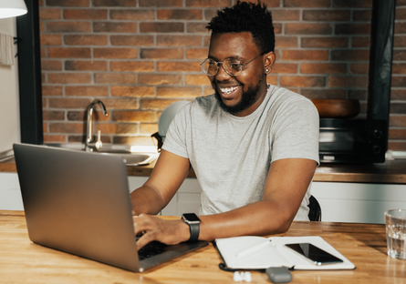 A man wearing a grey T-shirt working on a laptop