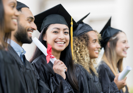 A group of college graduates wearing caps and gowns and one woman holding a diploma and smiling