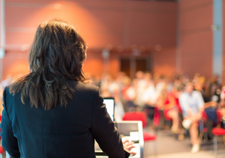 Image of female speaking to audience in a large room