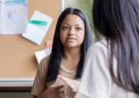 An image of a woman standing in front of a bulletin board talking to another woman
