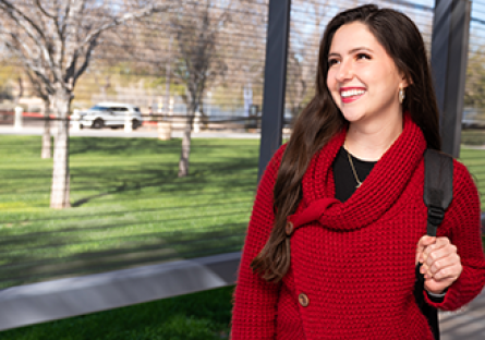 A happy, smiling student wearing a red sweater and backpack standing outside
