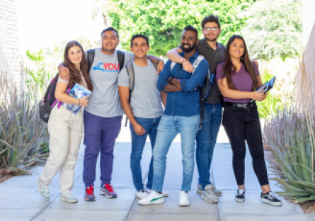 Six college students standing together  outside wearing backpacks and holding books
