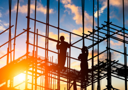 Stock photo of construction workers standing on scaffolding as the sun rises