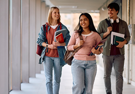 A stock photo of three college students walking down a hallway