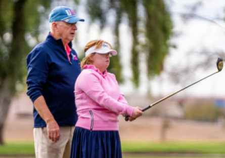 Joe Bockerstette standing bending his daughter Amy Bockerstette who is holding a golf club.