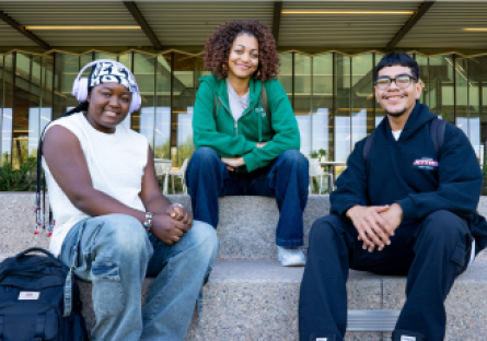 Three EMCC students sitting on steps outside of an entrance of a college building.