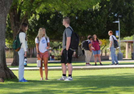 Three MCC students standing outside under a tree with three additional students in the background.