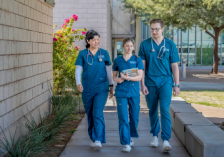 Three CGCC allied health students wearing blue medical scrubs walk together on the college campus.