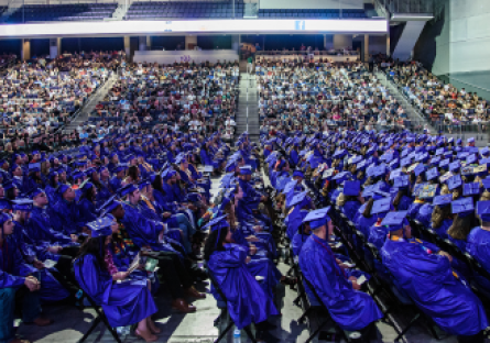 College graduates wearing royal blue caps and gowns seated in an auditorium.