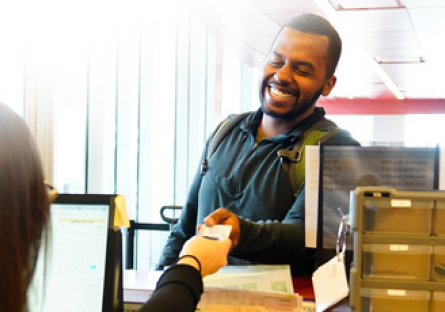 Man wearing a blue hoodie and backpack smiles as he is being handed a ticket.