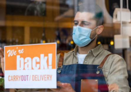 Shop owner holding up sign that reads, "We're back!"