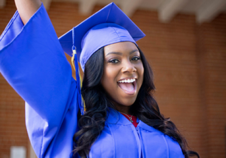 Image of a happy woman with her arm raised wearing a cap and gown