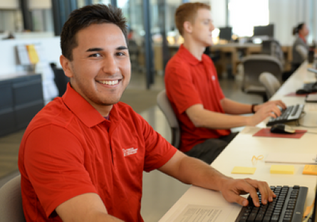 Image of Mesa Community College students wearing red polo shirts and using computers