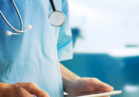 A close up image of a doctor wearing blue scrubs and stethoscope and holing a tablet